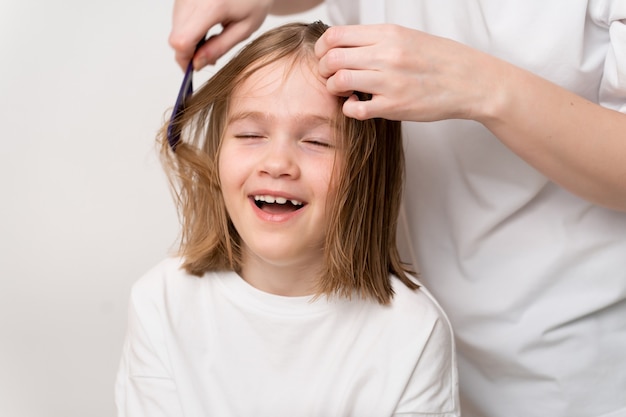 Woman combs and does the hair of a funny small girl on a white background. Mommy is a hairdresser. saving money at a beauty salon. shampoos and cosmetics for children's hair.