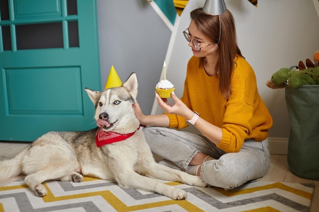 A woman congratulates pet dog on birthday the dog licks the cream from the birthday cake