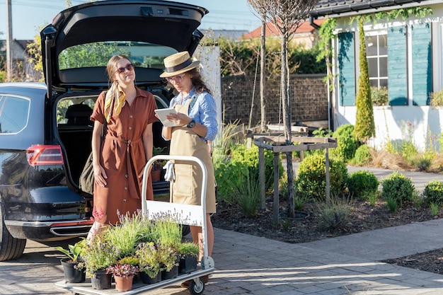 A woman consults a female gardener about plants before buying them in a garden center near car