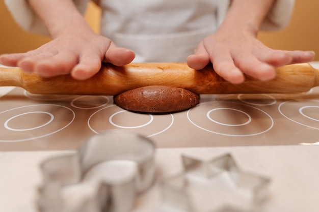 Woman cook with rolling pin kneads ginger dough for baking cookies on beige table confectionery concept