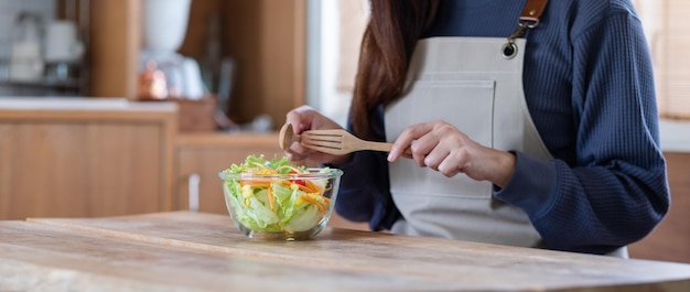 A woman cooking and eating fresh mixed vegetables salad at home