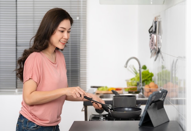 Woman cooking and preparing food according to a recipe on a tablet computer in the kitchen at home