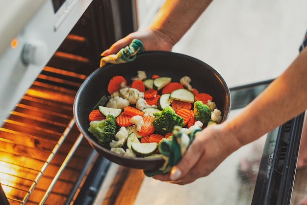 Woman cooking vegetables puting pan with vegetables to the oven. Home cooking concept.