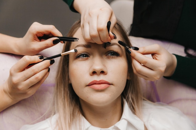 A woman corrects the shape of her eyebrows in a beauty salon 4 hands do eyebrow correction