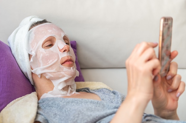 Woman in cosmetic mask with phone lies on sofa close-up