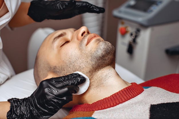 A woman cosmetologist prepares equipment for carrying out a procedure for a man in a chair