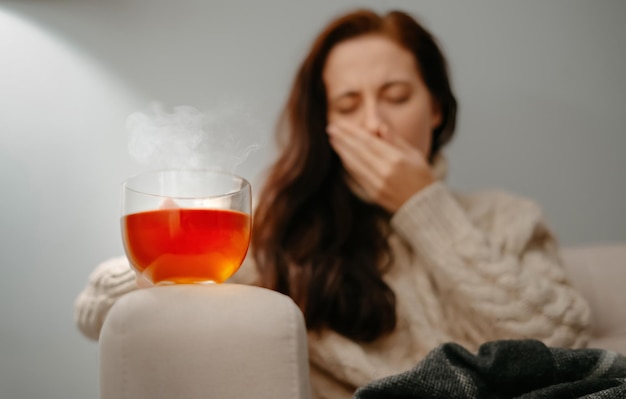 Woman coughs in hand with sore throat holding hot medicinal tea