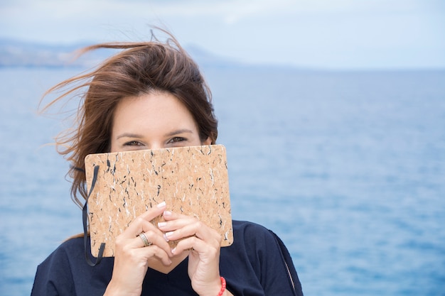 Woman covers her face shyly with her notebook where she has written all her confidences.