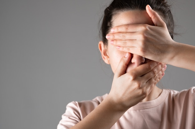 The woman covers her mouth and eyes with her hands.