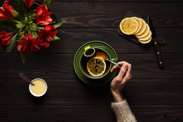 Woman in a cozy beige sweater drinking a big cup of hot tea with lemon and honey on wooden background overhead shot