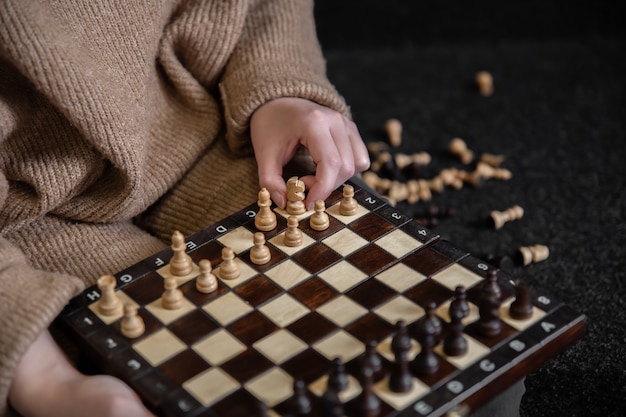 Woman in cozy sweater places wooden chess pieces on a chessboard.