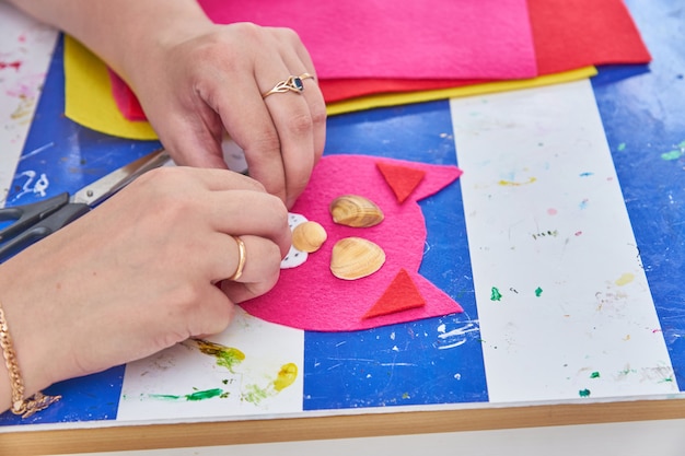 Woman create a cat from red felt and sea shells at the workshop