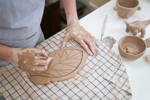 Photo woman creates pattern on a leaf shaped piece of clay by hands in artistic studio