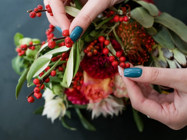 Woman creating autumn flower and berries arrangement on dark background. Bouquet design and composition art ikebana.