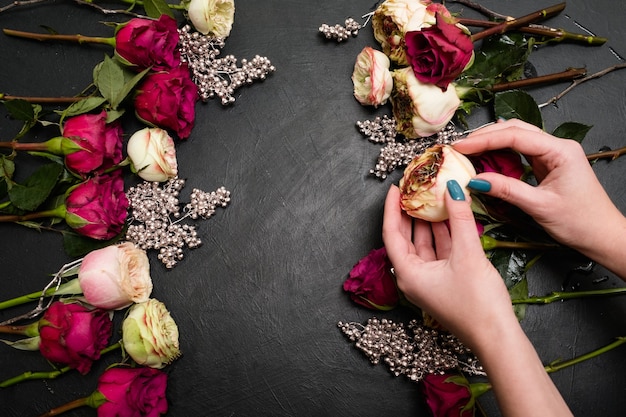 Photo woman creating a bouquet composition of red and pink roses on dark background. art of floristry and floral arrangements. beautiful design concept