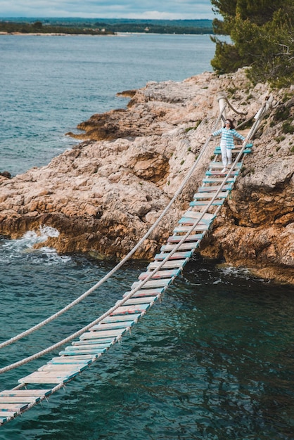 Woman crossing suspension bridge sea on background