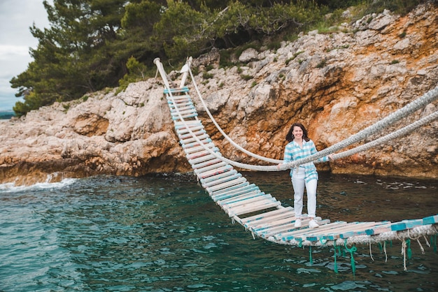 Woman crossing suspension bridge sea on background