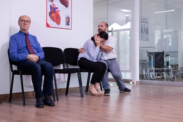 Woman crying in husband arms sitting in hospital waiting area