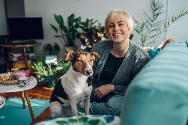 Woman cuddling and playing with her dog at home on the couch