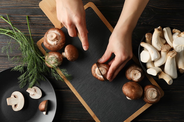 Woman cuts champignon on cutting board with mushrooms, top view