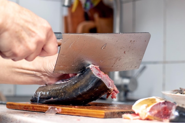 A woman cuts fish with a large knife at home in the kitchen