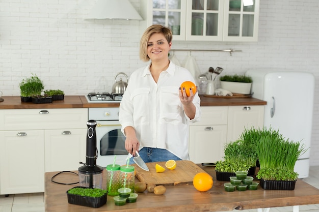 Woman cuts a lemon in the kitchen on the table for a vitamin smoothie made of microgreen and fruit