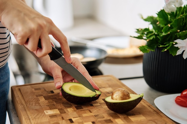 Woman cutting avocado on cutting board to prepare breakfast