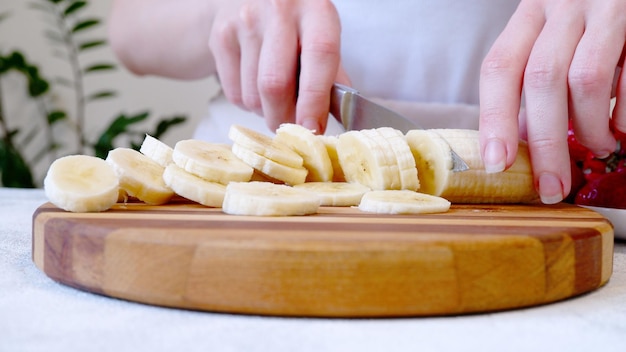 Woman cutting banana on wooden board and preparing smoothie or milkshake