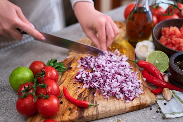 Woman cutting and chopping onion by knife on wooden board