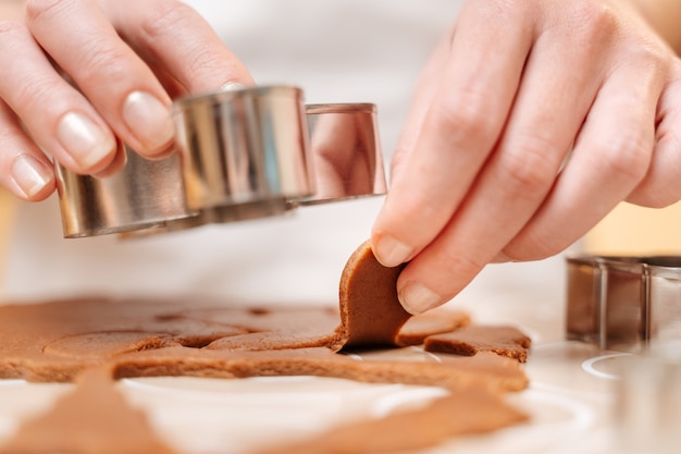 A woman cutting gingerbread dough men with a christmas cookie cutter closeup