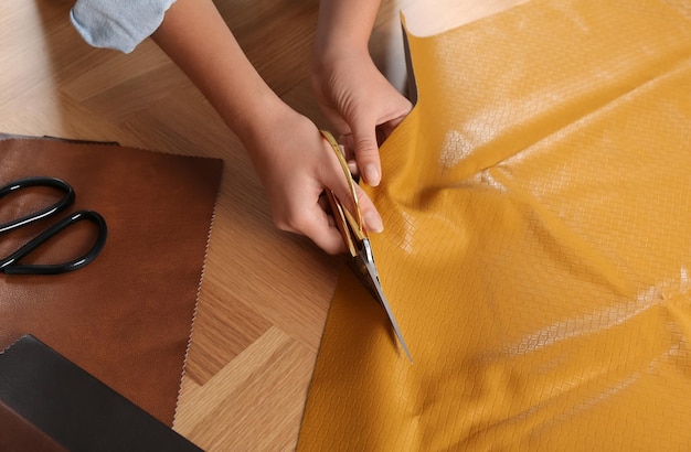 Photo woman cutting orange leather with scissors at wooden table closeup