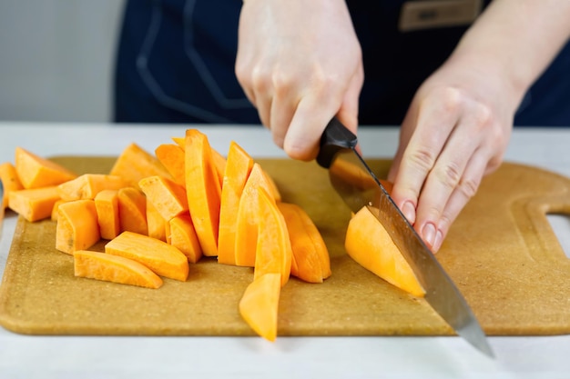 Woman cutting with knife sweet potato into wedges on wooden board close up