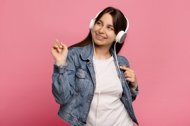 woman dances in rhythm of melody, listens loud song in headphones isolated on pink