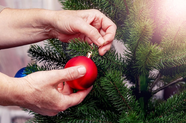 A woman decorates a Christmas and New Year tree A New Year's ball in the hands of a woman near a Christmas tree