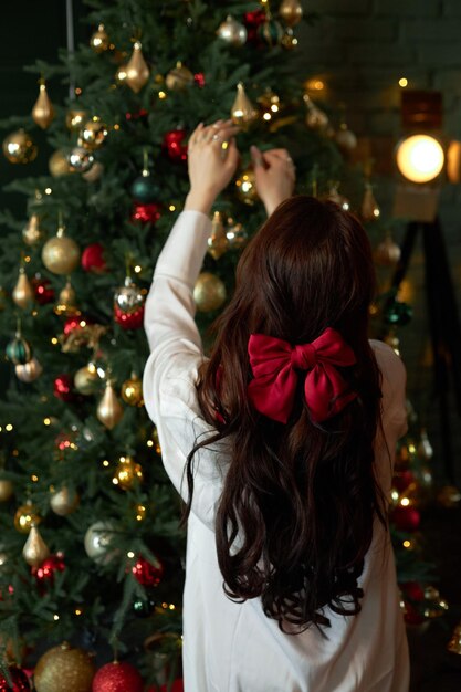 Woman decorates a Christmas tree with garlands and toys at home Morning before Christmas New Year 2023