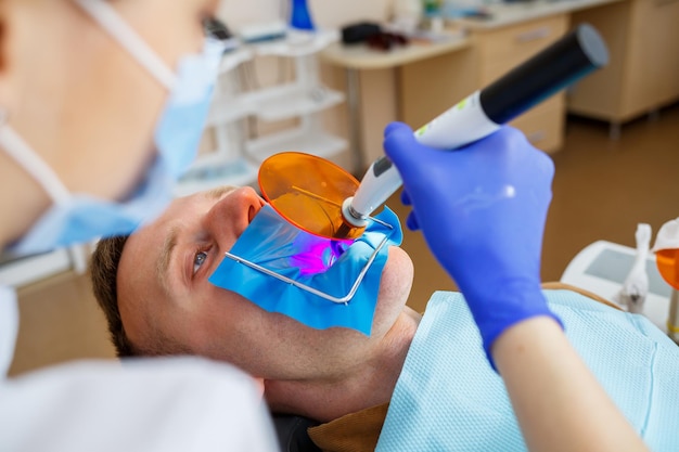 Woman dentist examines the patient with instruments in the dental clinic. The doctor makes dental treatment on the teeth of a person in the dentist's chair. Selective focus