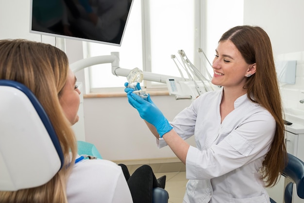 A woman dentist shows a young girl a model of an artificial jawThe dentist shows how to properly care for the oral cavity the cost and consequences