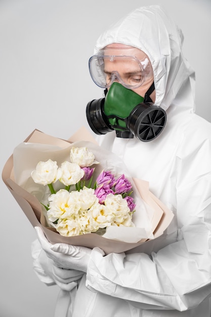 Woman disinfectant in a respirator, protective suit, glasses and gloves with a bouquet of flowers.