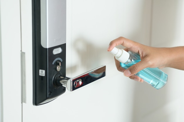 Woman disinfecting the Door knob by spraying a blue sanitizer from a bottle, Prevent covid19, corona virus.