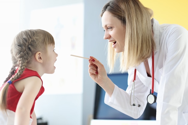 Woman doctor examining throat of little girl with spatula in clinic