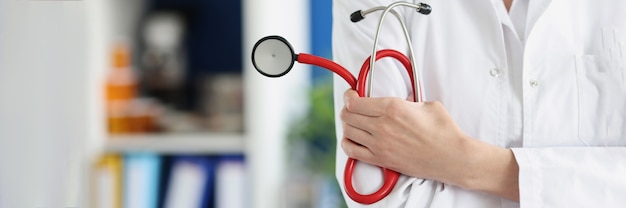 Woman doctor holding red stethoscope in clinic closeup