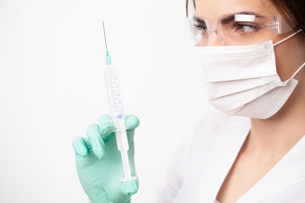 Woman doctor in medical mask picks up syringe to give an injection.