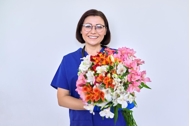 Woman doctor nurse in blue with bouquet of flowers on light background