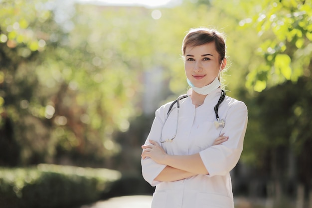 Woman doctor or nurse in a face protective mask in the park among the trees.