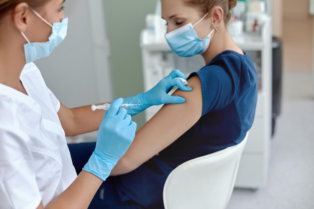 Woman doctor or nurse giving shot or vaccine to patient shoulder