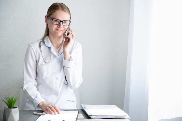 Woman doctor in an office consults patient by phone. Healthcare specialist at the table. Authentic people.