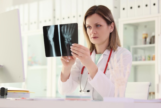 Woman doctor studies xray picture of patient arm sitting at table in clinic premise