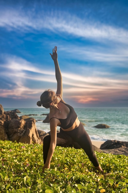 Woman does asana yoga for healthy lifestyle on tropical sea or ocean beach outdoors on sunset