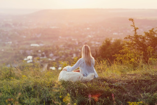 woman and a dog sitting on the hill and enjoying countryside landscape