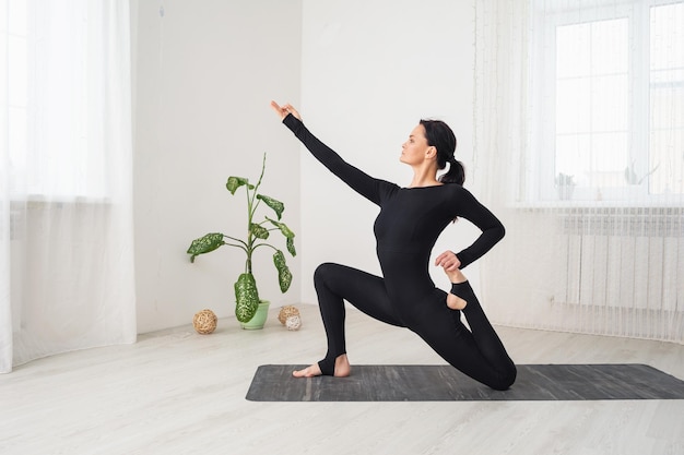 Woman doing anjaneyasana exercise with virasana low lunge pose sitting on a mat in a room